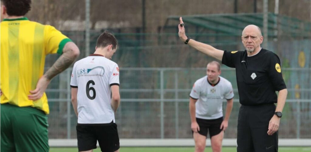 Jan Meijsen als scheidsrechter op het veld, terwijl hij ook de gezondheid van de spelers waarborgt als Rode Kruis-hulpverlener.