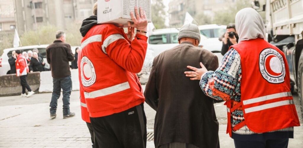 Vrijwilligers van het Rode Kruis helpen een man op weg naar zijn huis.