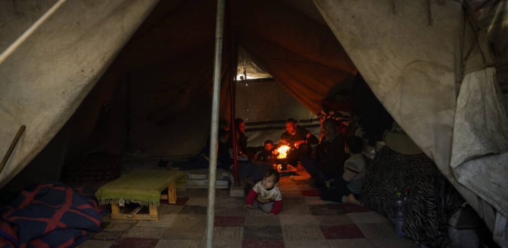 Een gezin kruipt dicht bij elkaar rond een geïmproviseerd vuur om zich te warmen tijdens zware regenval in het vluchtelingenkamp in Jabalia, Gaza.