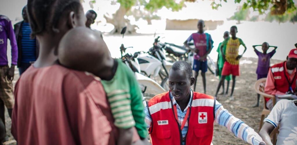 Een jonge moeder houdt haar verzwakte zoontje dicht tegen zich aan terwijl een hulpverlener van het Soedanese Rode Kruis medicijnen en ORS geeft om te herstellen van dagenlange diarree.
