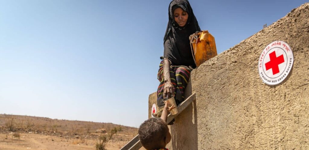 Wereldwaterdag foto vrouw geeft water aan kindje uit waterbron Rode Kruis