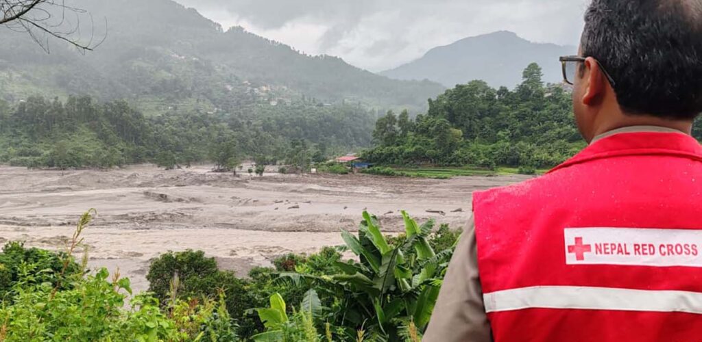 Een vrijwilliger van het Nepalese Rode Kruis kijkt bedroefd naar de verwoesting van de overstroming