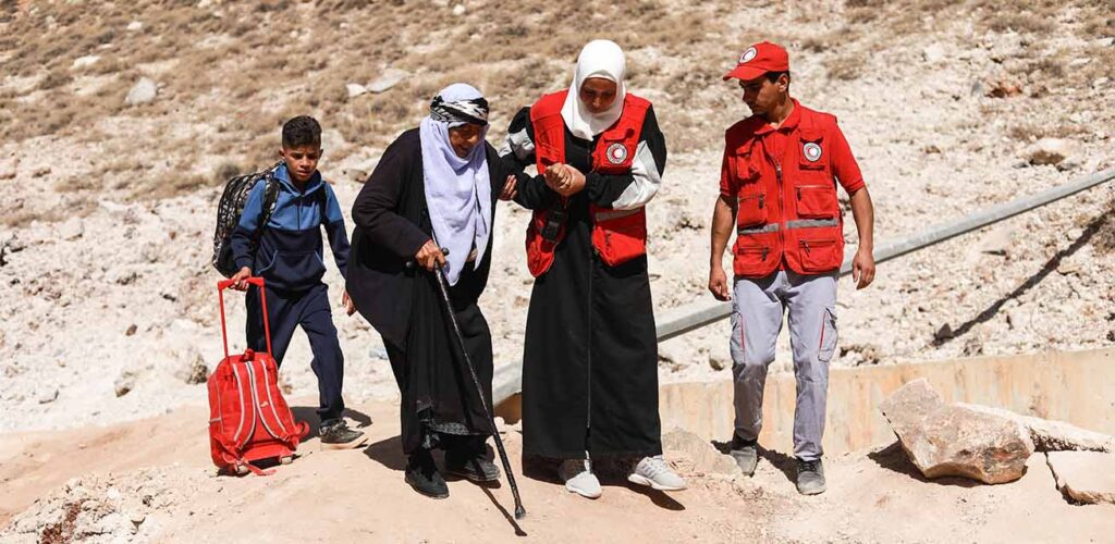 Hulpverleners van de Syrische Rode Halve Maan ondersteunen mensen die de grens tussen Libanon en Syrië oversteken