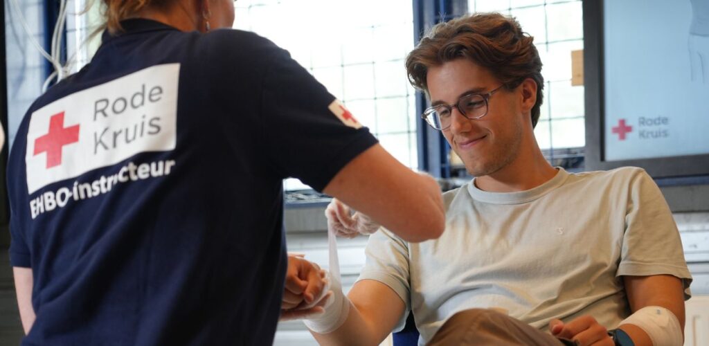 Karel oefent tijdens een EHBO-cursus van het Rode Kruis met het aanbrengen van verband.