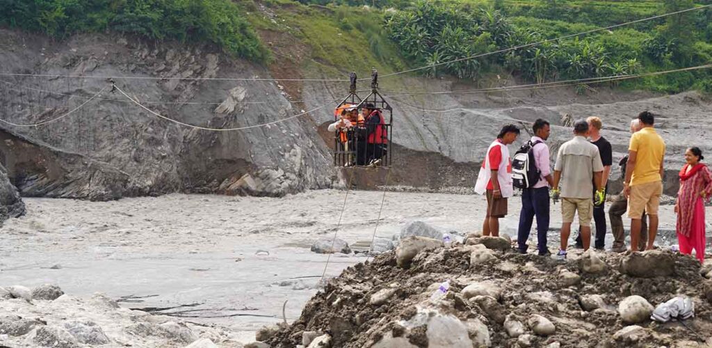 Vrijwilligers van het Nepalese Rode Kruis helpen mensen de rivier over via een tijdelijke kabelverbinding